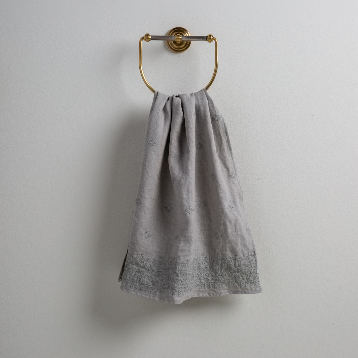 Mineral: guest towel draped through a decorative brass towel ring against a white background.