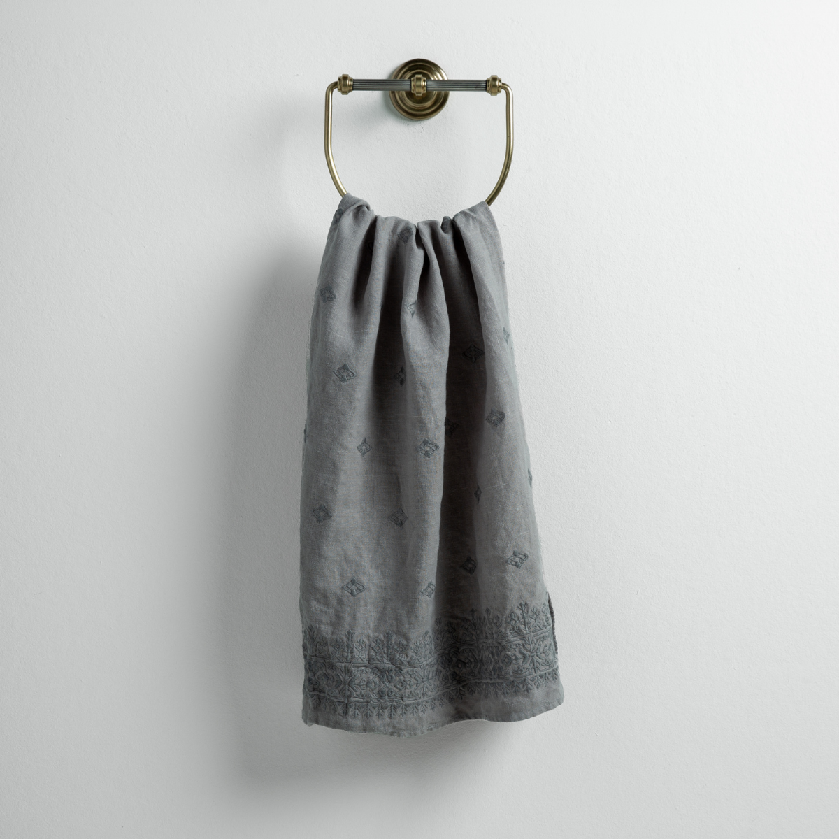 Moonlight: guest towel draped through a decorative brass towel ring against a white background.