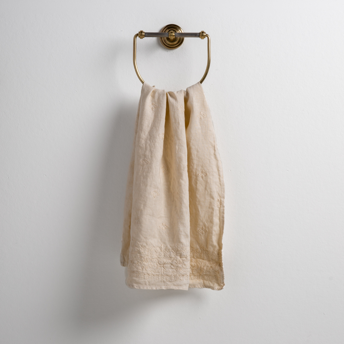 Parchment: guest towel draped through a decorative brass towel ring against a white background.