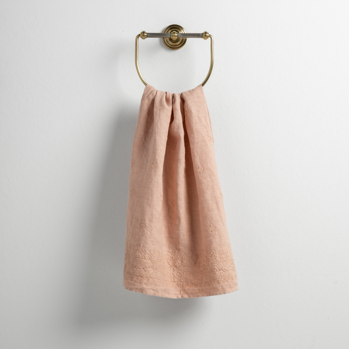 Rouge: guest towel draped through a decorative brass towel ring against a white background.