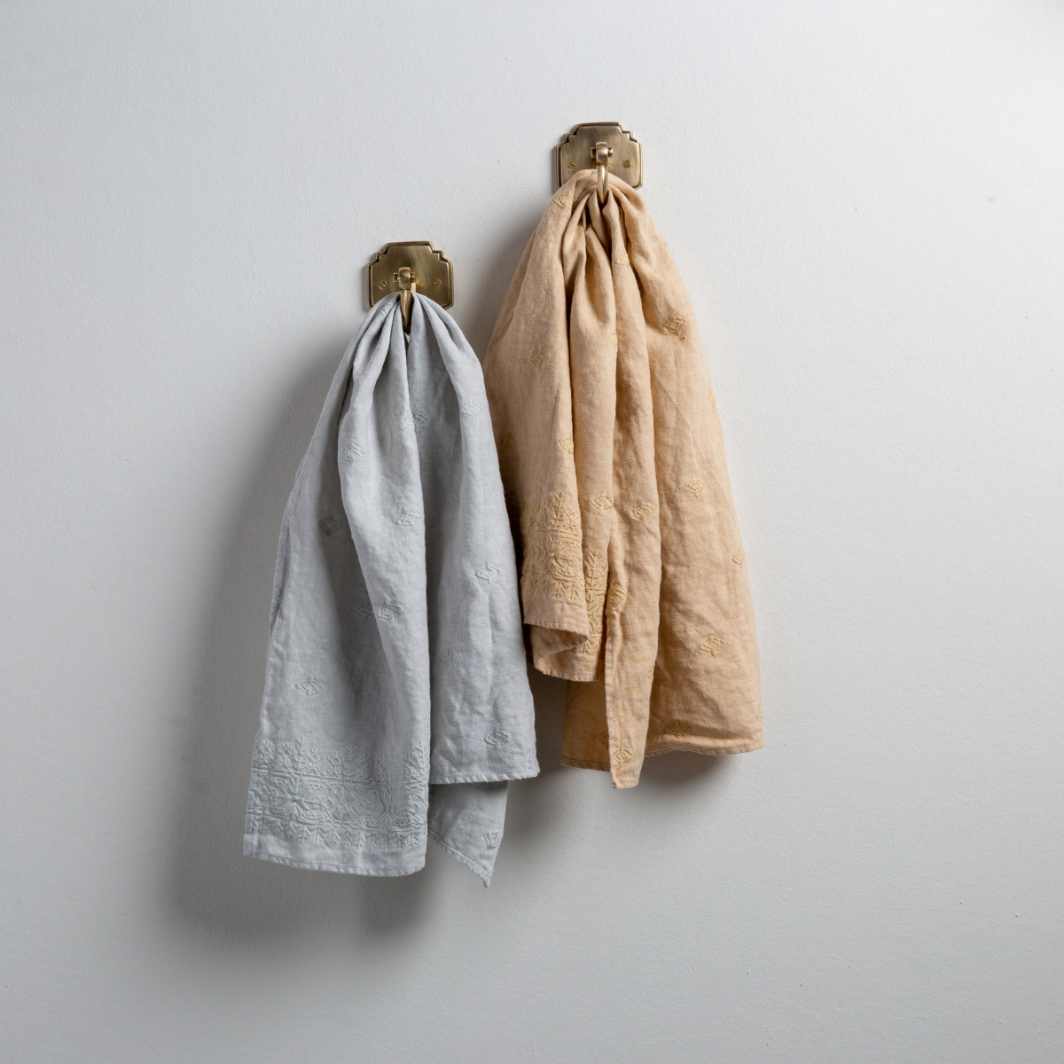 : Two Ines guest towels, draped over decorative hooks against a white wall - cloud and honeycomb.