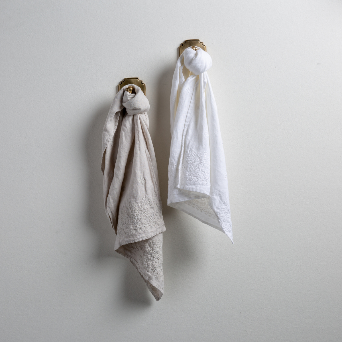: Two Ines guest towels, draped over decorative hooks against a white wall - sterling and white.