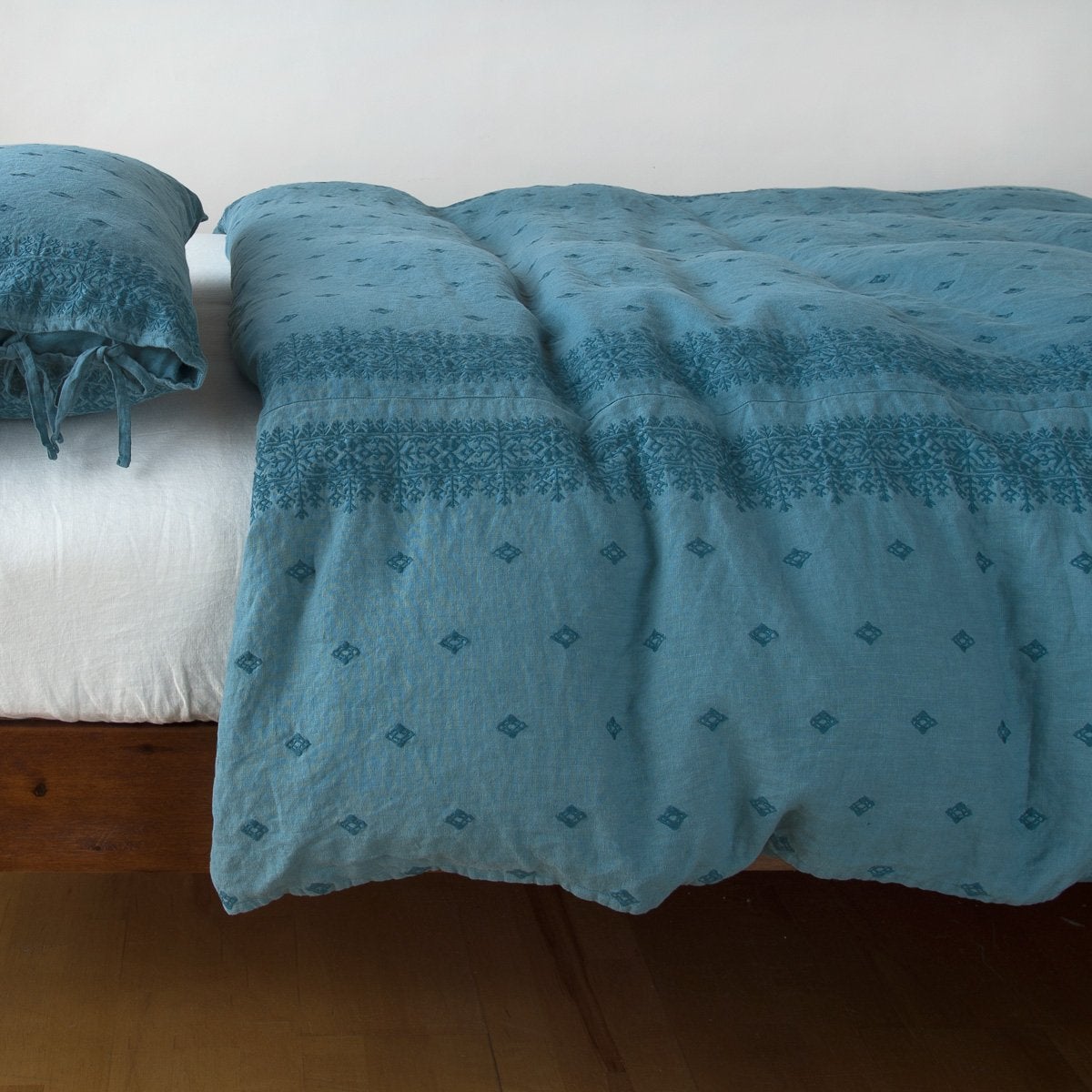 Cenote: lightly rumpled duvet cover on a monochromatic bed against a white background - side view.