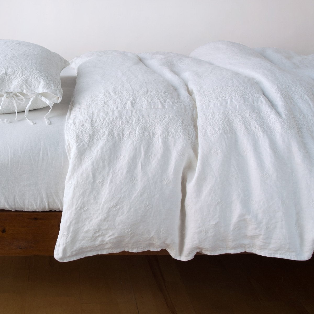 White: lightly rumpled duvet cover on a monochromatic bed against a white background - side view.