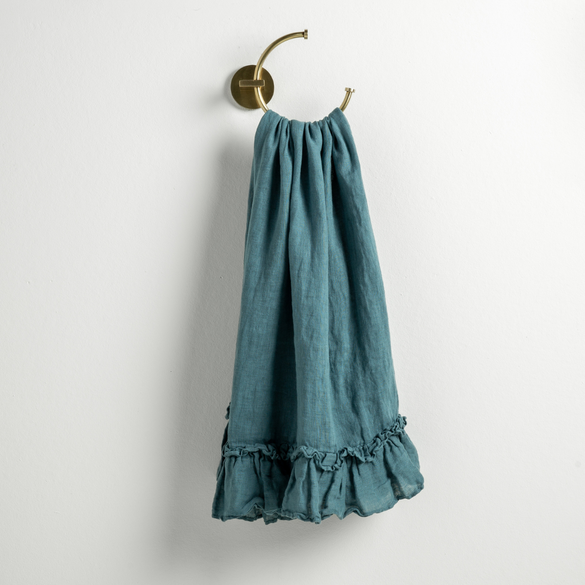 Cenote: guest towel draped through a decorative brass towel ring, against a white wall.