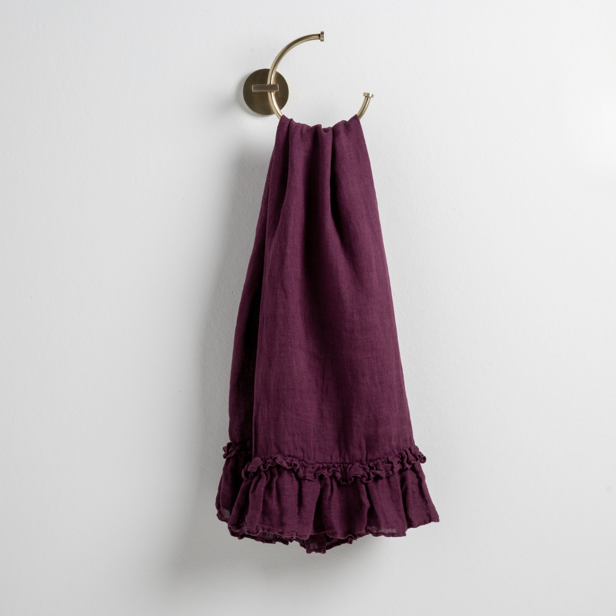 Fig: guest towel draped through a decorative brass towel ring, against a white wall.