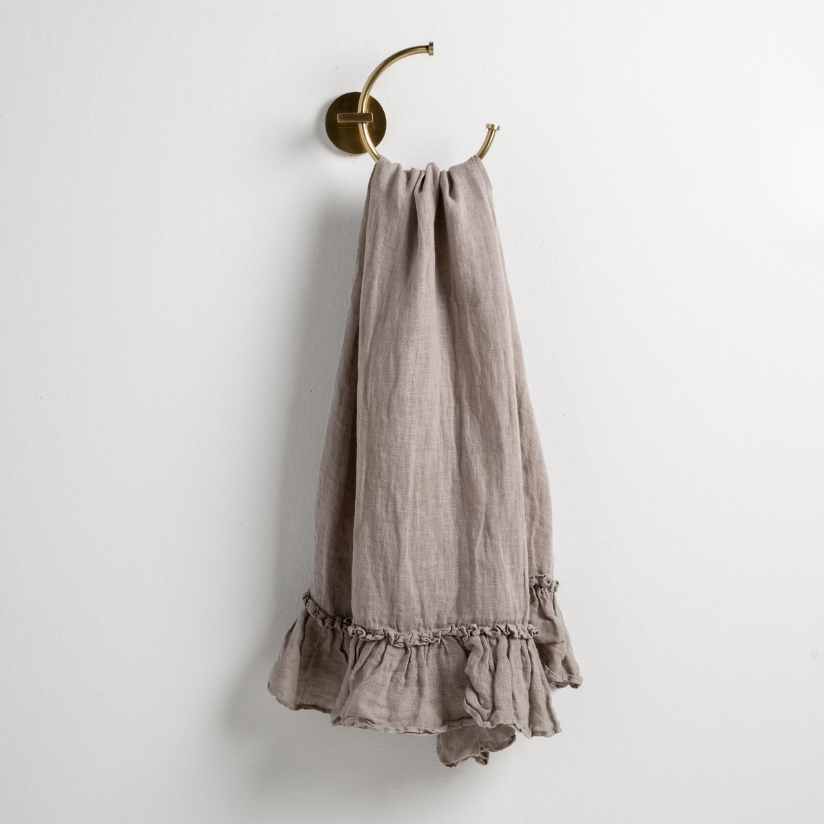 Fog: guest towel draped through a decorative brass towel ring, against a white wall.