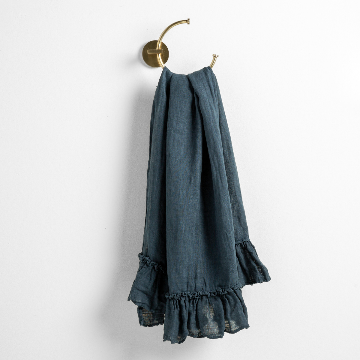 Midnight: guest towel draped through a decorative brass towel ring, against a white wall.