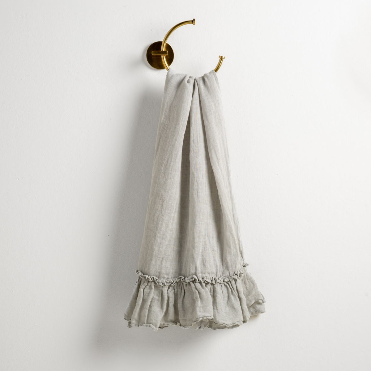 Mineral: guest towel draped through a decorative brass towel ring, against a white wall.