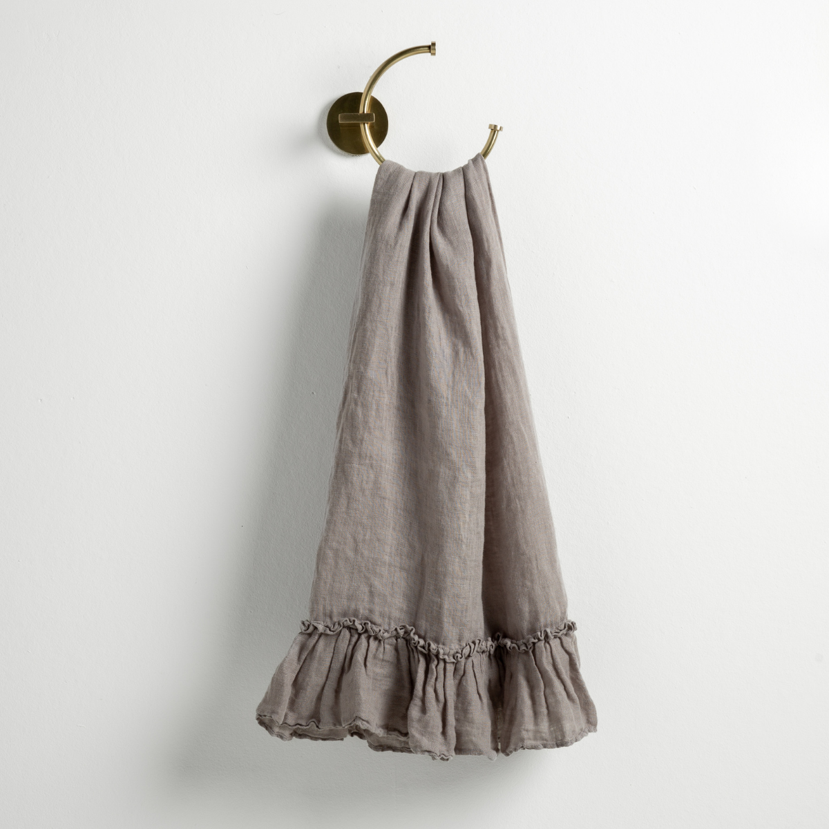 Moonlight: guest towel draped through a decorative brass towel ring, against a white wall.