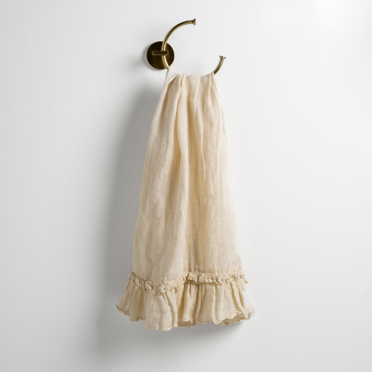 Parchment: guest towel draped through a decorative brass towel ring, against a white wall.