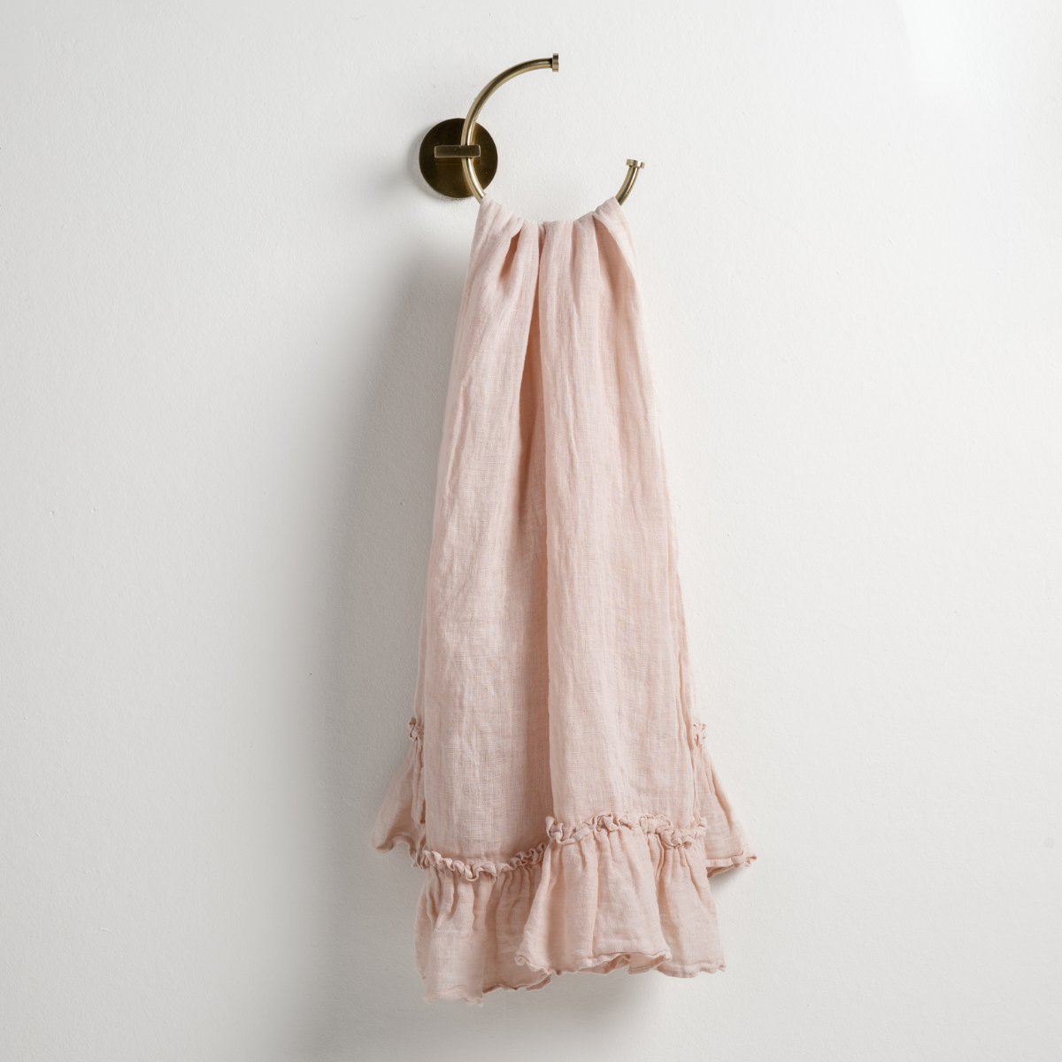 Pearl: guest towel draped through a decorative brass towel ring, against a white wall.