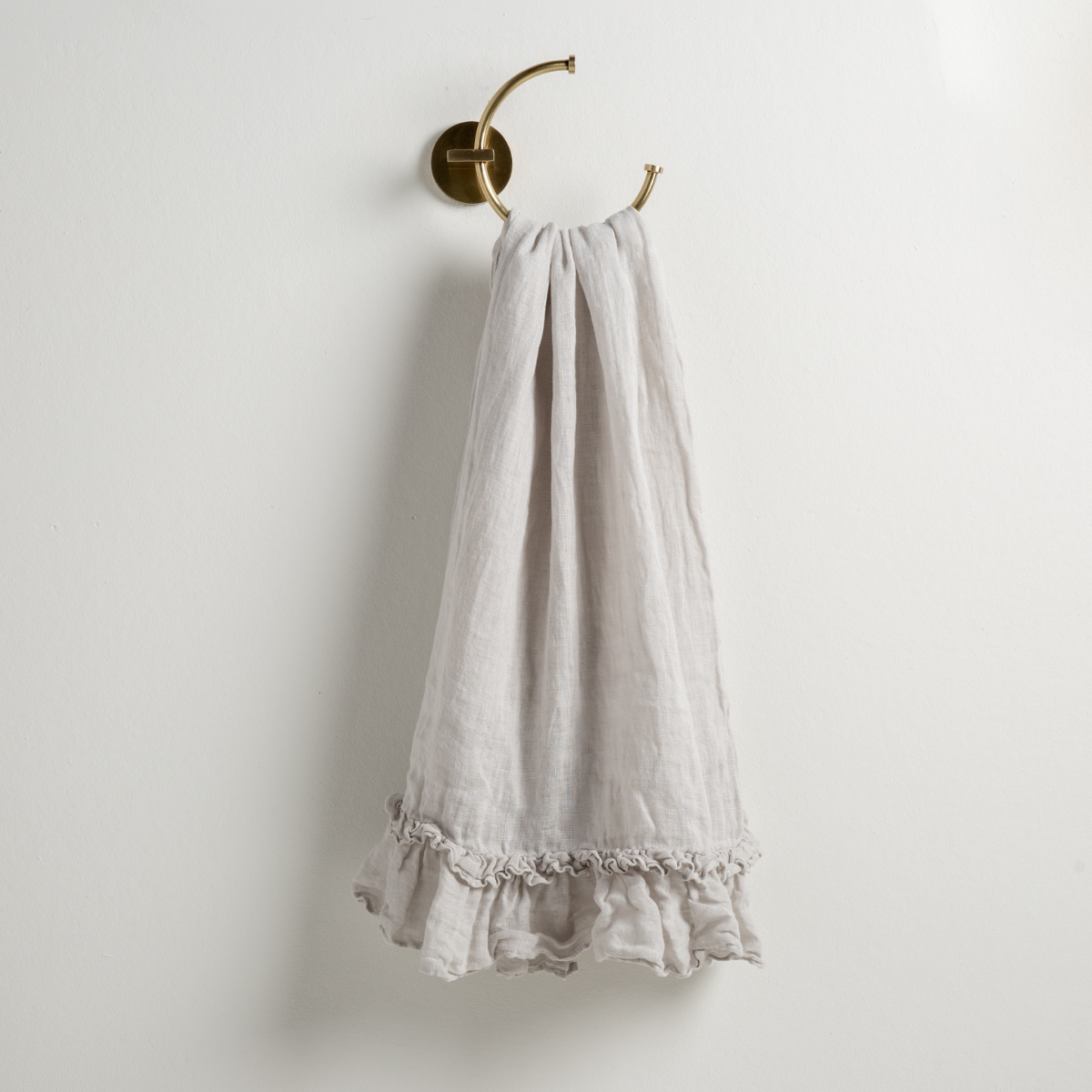 Sterling: guest towel draped through a decorative brass towel ring, against a white wall.
