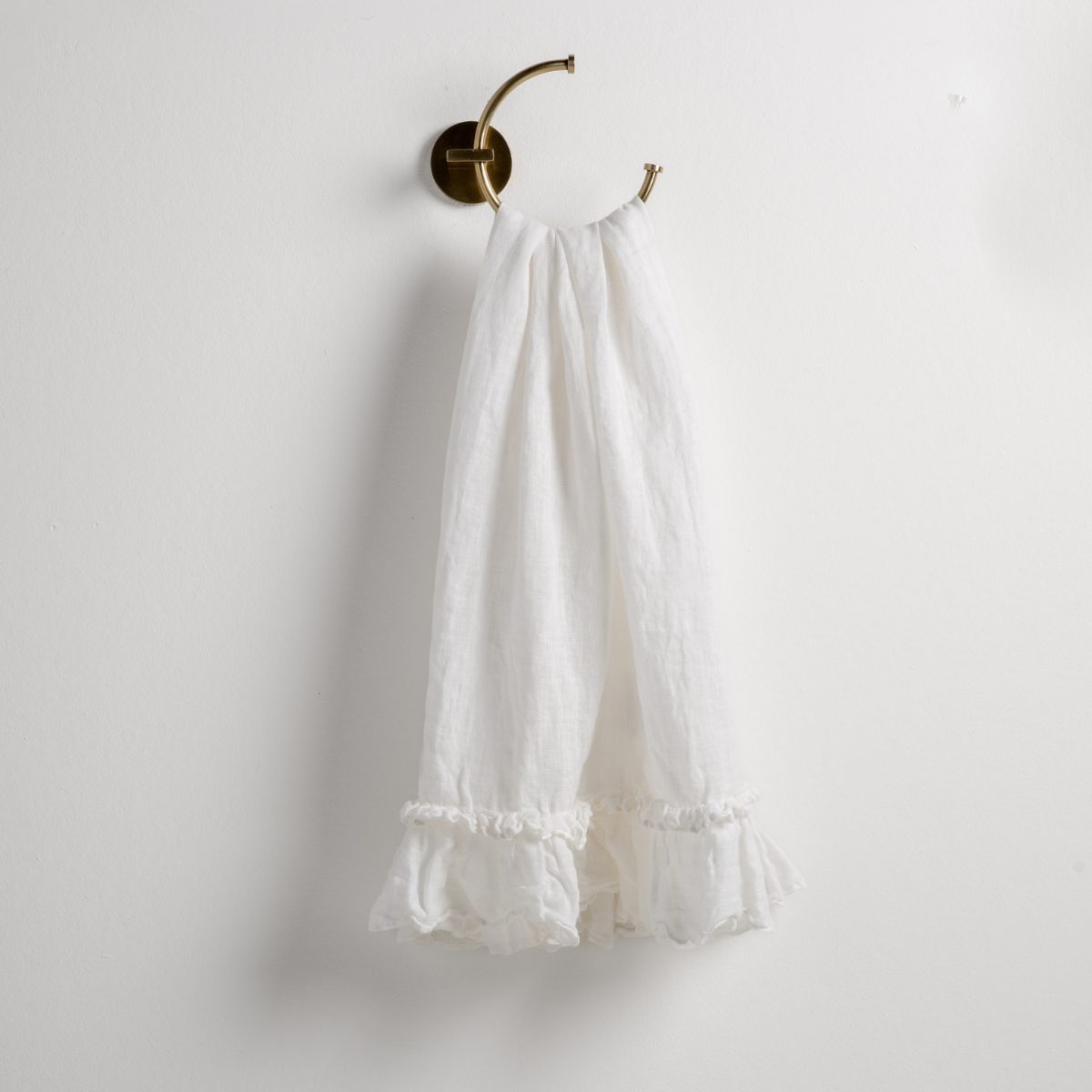 Winter White: guest towel draped through a decorative brass towel ring, against a white wall.