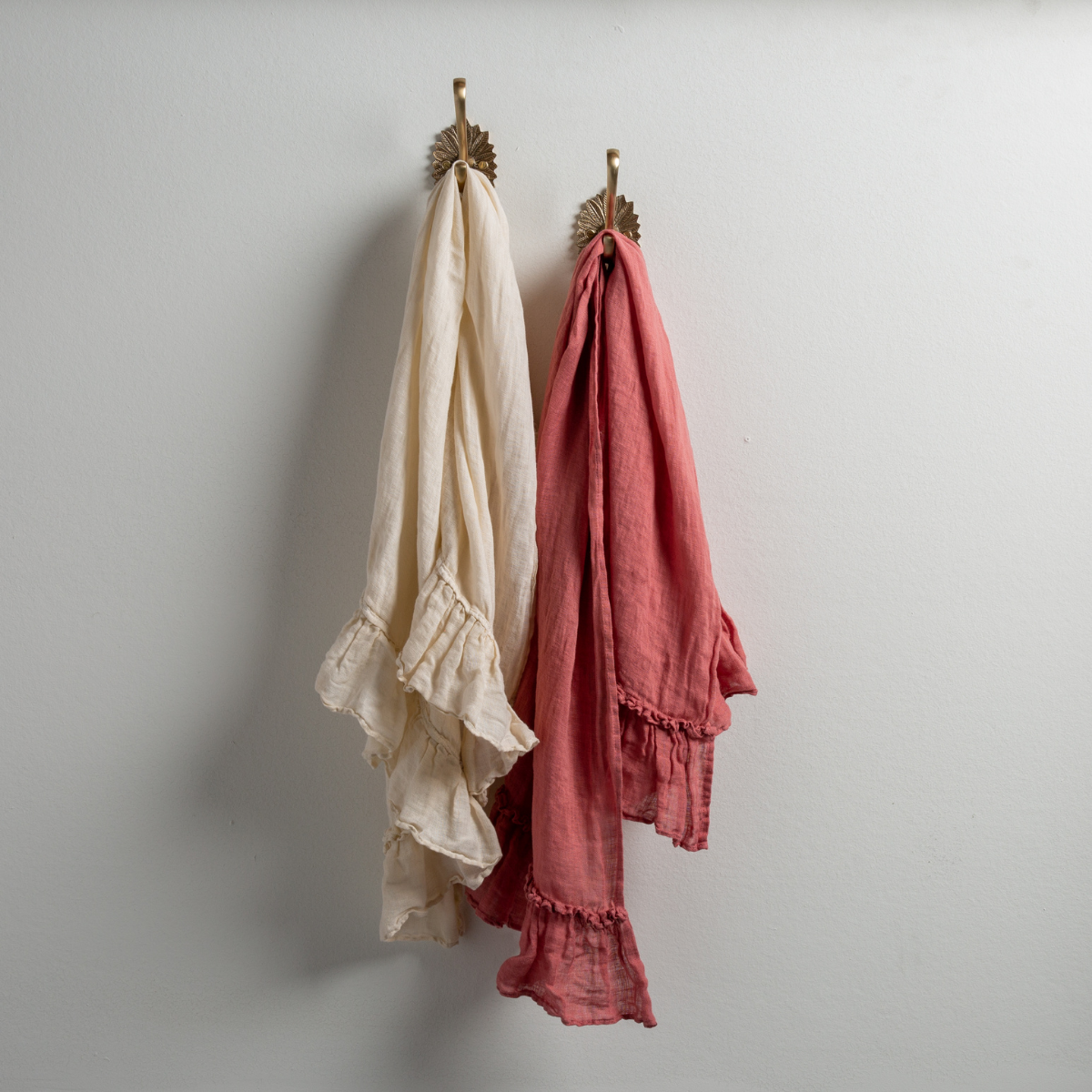 : Two Linen Whisper guest towels, draped over decorative hooks against a white wall - parchment and poppy.