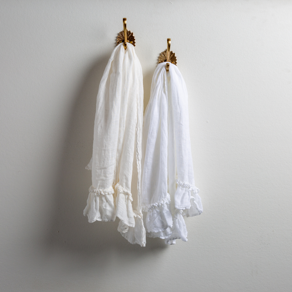 : Two Linen Whisper guest towels, draped over decorative hooks against a white wall - white and winter white.