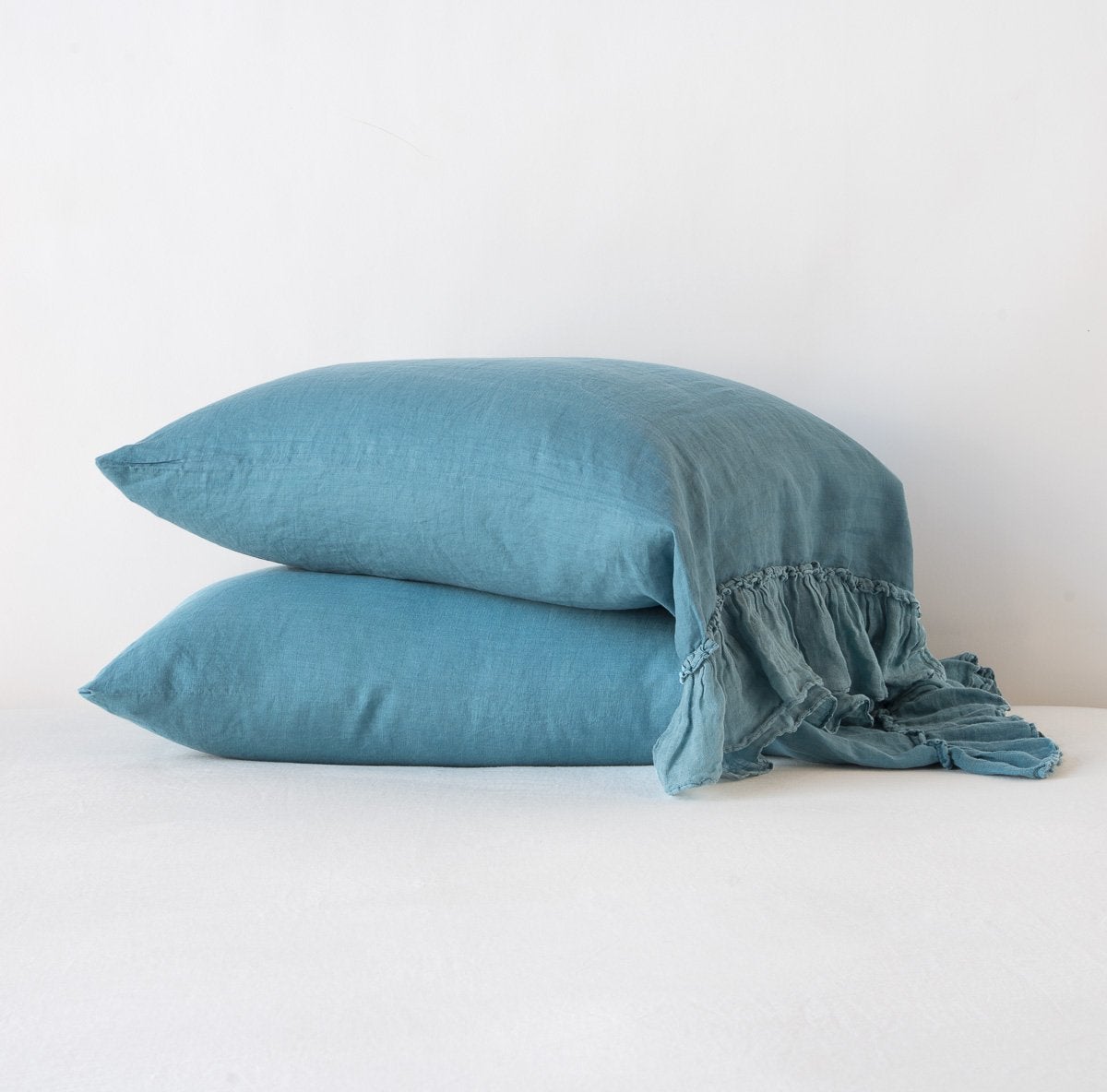 Cenote: Two sleeping pillows stacked at a slight angle against a plain background, showcasing ruffle trim detail - side view.