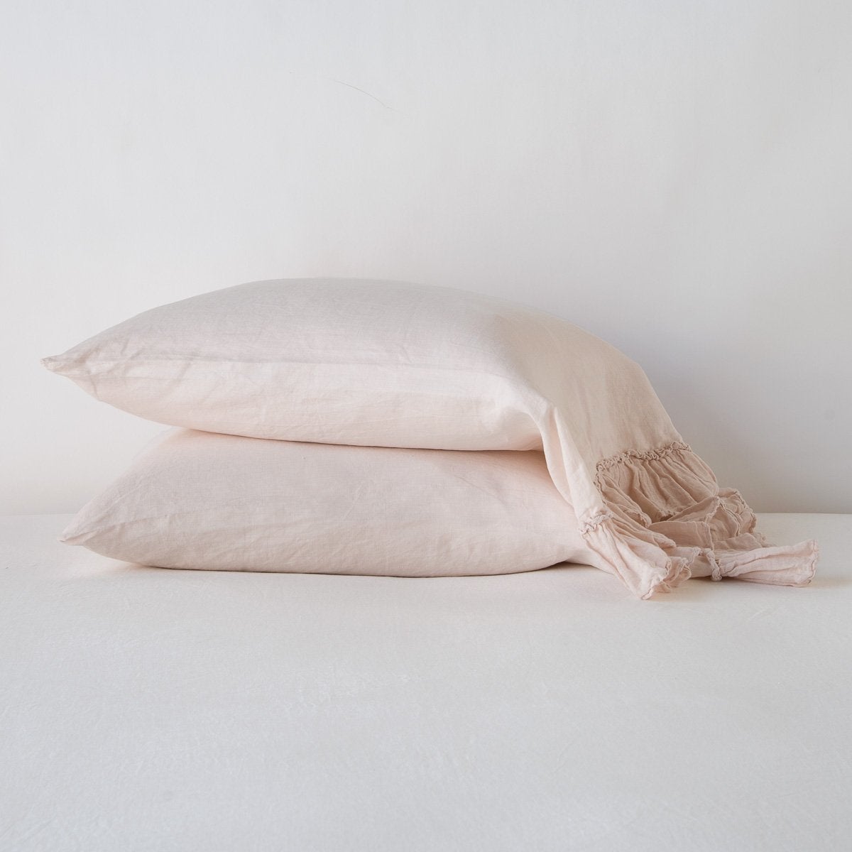 Pearl: Two sleeping pillows stacked at a slight angle against a plain background, showcasing ruffle trim detail - side view.
