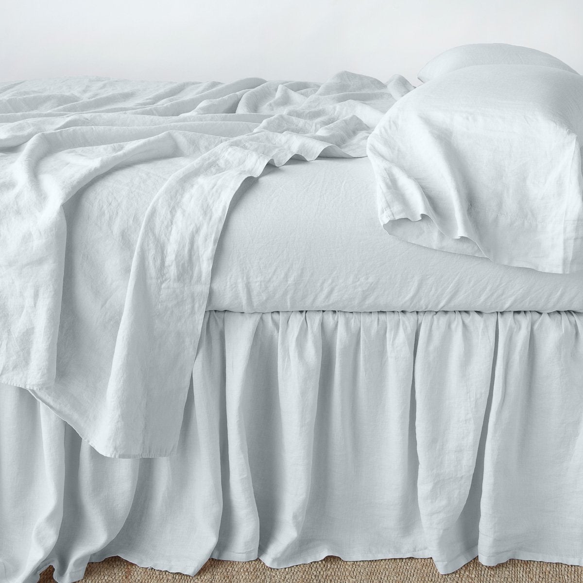 : Linen bed skirt in cloud, with matching rumpled sheets and sleeping pillows - side view.