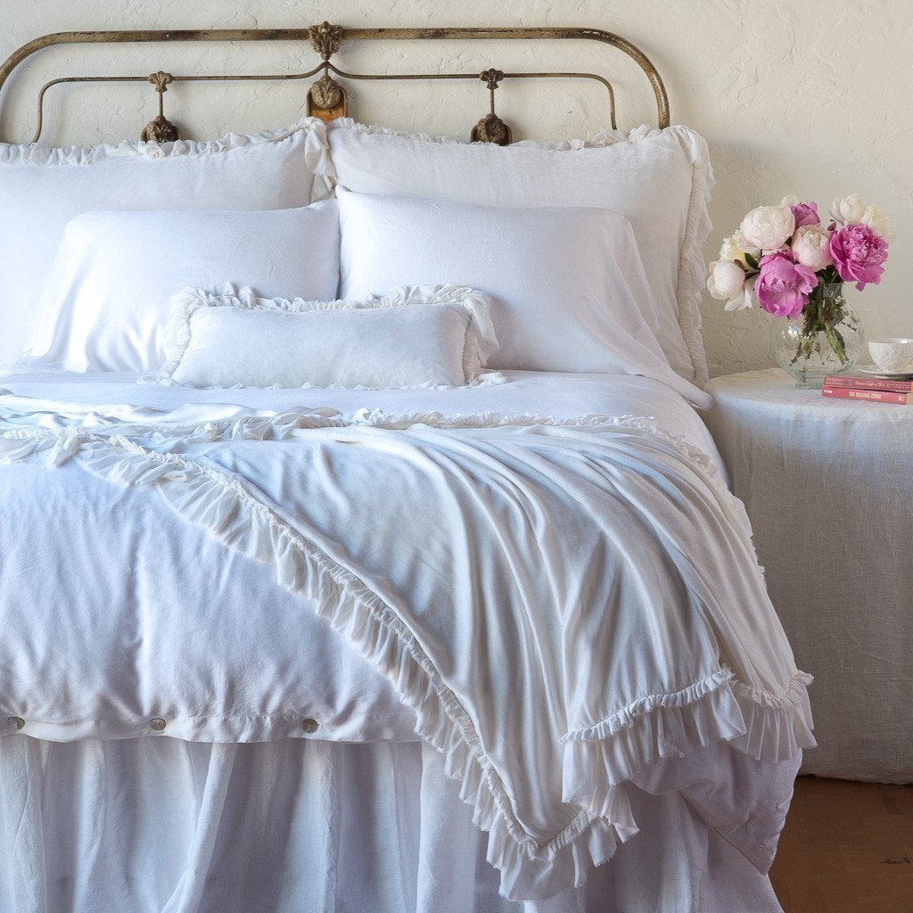White: throw blanket draped over the end of a white bed, shown with matching accent pillow - end of bed view.