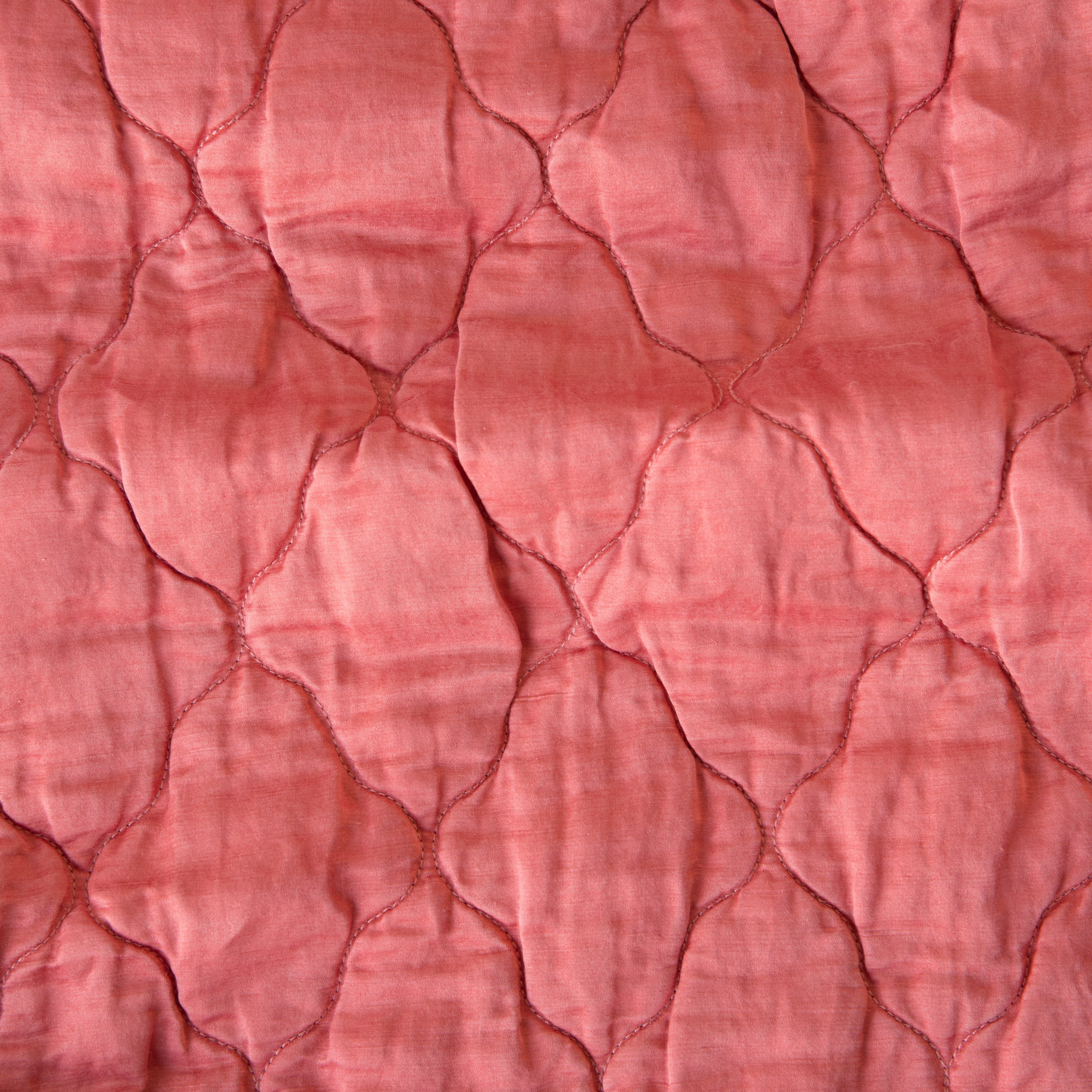Poppy: Close-up of Luna silk charmeuse quilting in poppy, a warm coral pink.