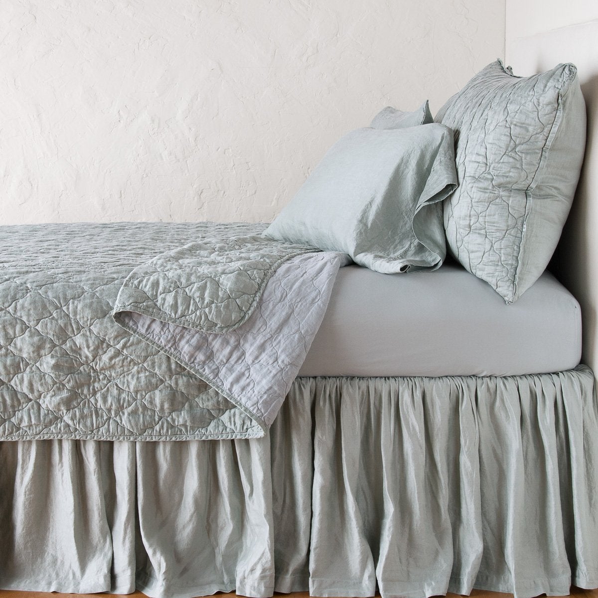 : Luna coverlet neatly folded back to reveal linen reverse, on a monochromatic bed - eucalyptus, side view.