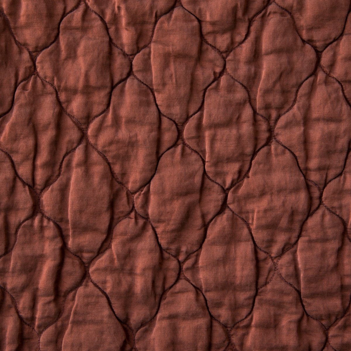 Mahogany: Close-up of Luna silk charmeuse quilting in mahogany, a deep, earthen, reddish brown.