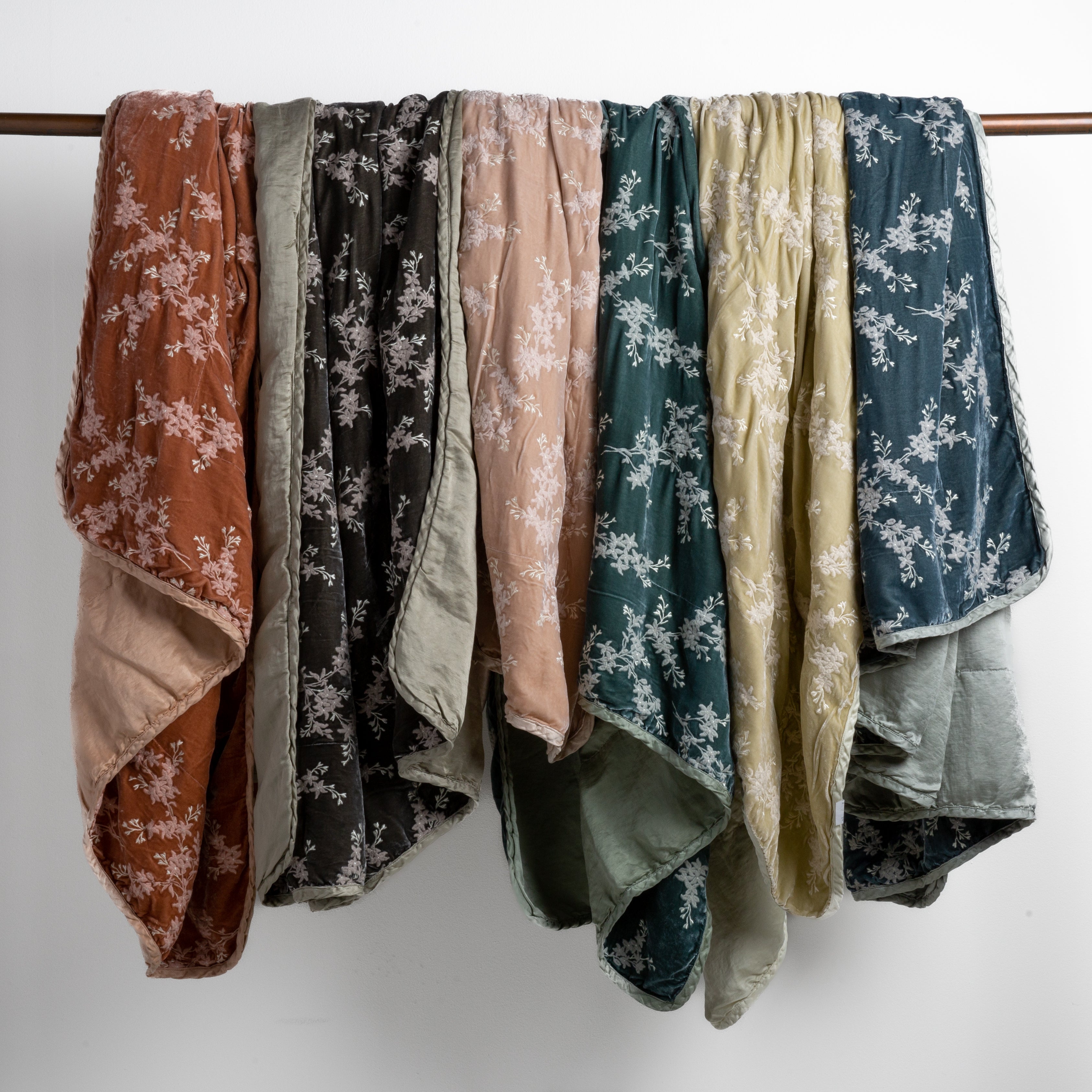 : embroidered silk velvet blankets with charmeuse backs and trimsdraped over a copper bar straight on against a white background.