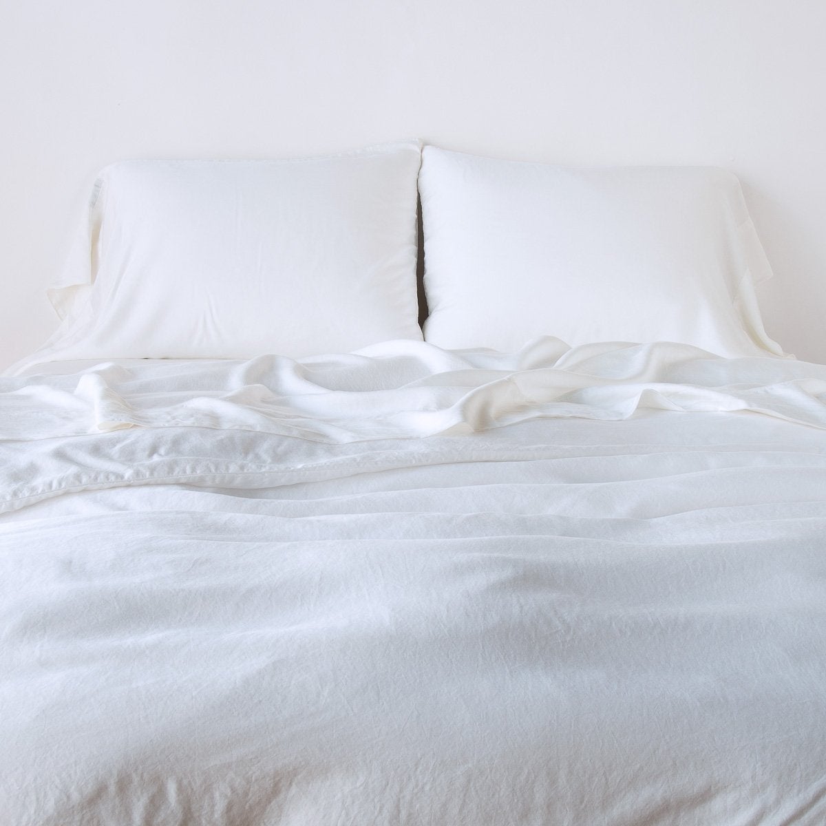 White: duvet cover with matching sleeping pillows and sheeting against a white wall - end of bed view.
