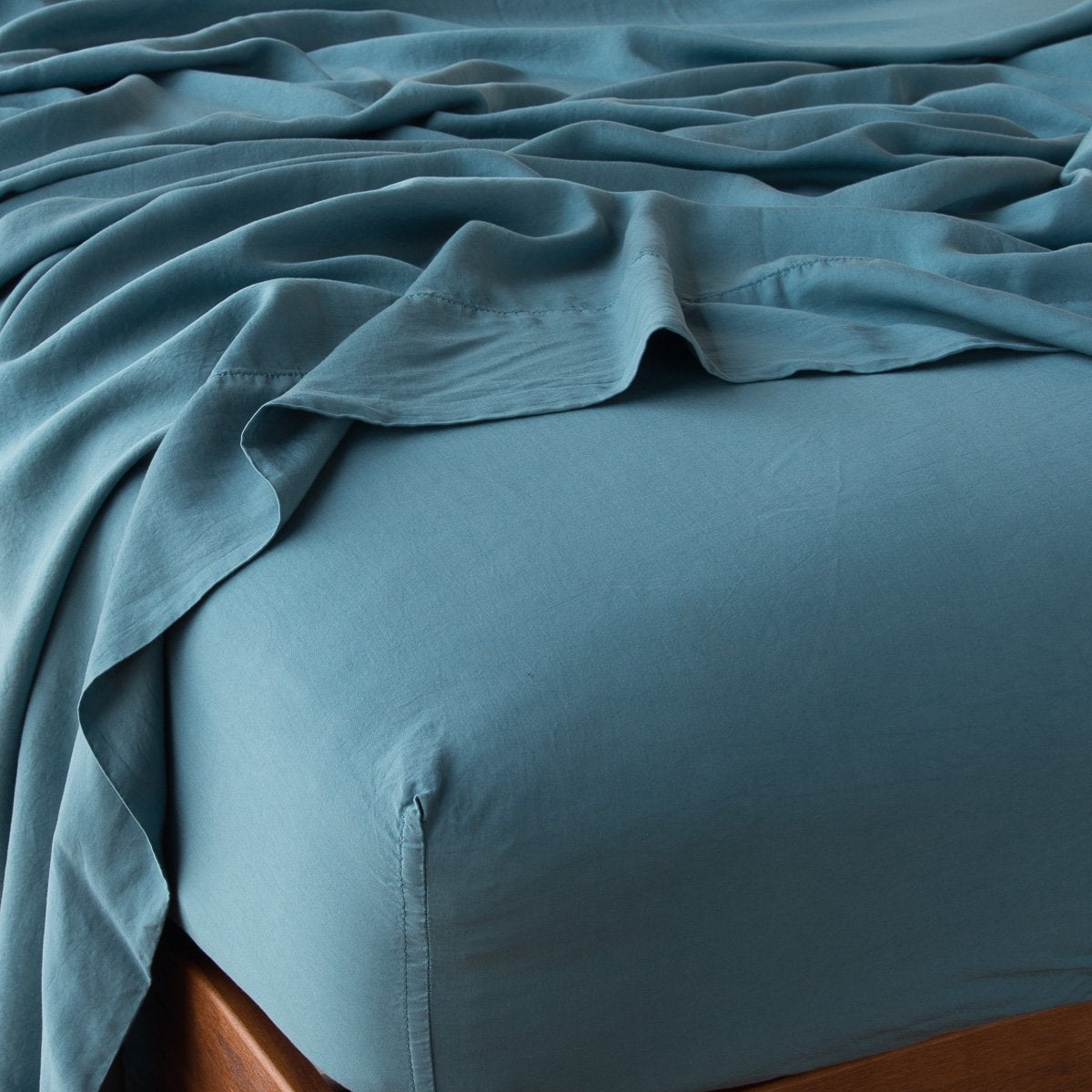 : Madera Luxe fitted sheet in cenote with matching rumpled flat sheet - shown from top corner.