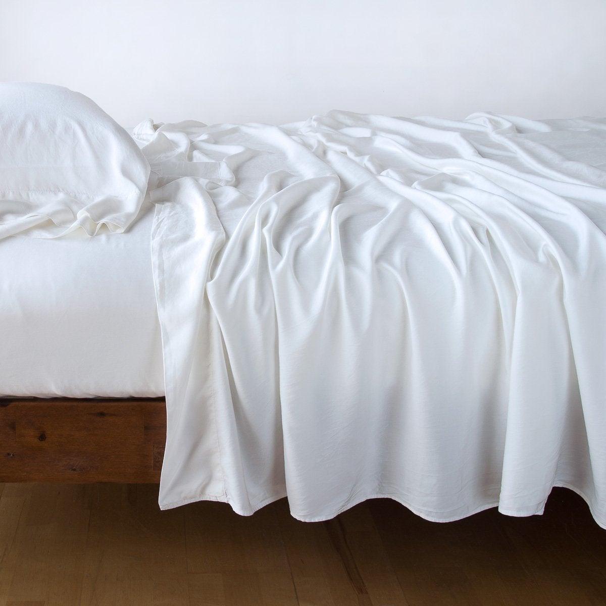 White: fitted sheet with matching rumpled flat sheet and sleeping pillow - side view.