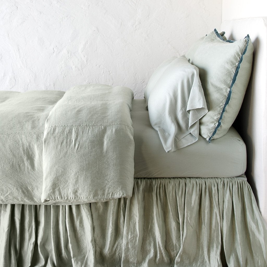 : Paloma bed skirt, layered under a matching duvet cover and monochromatic sheeting - eucalyptus, side view.