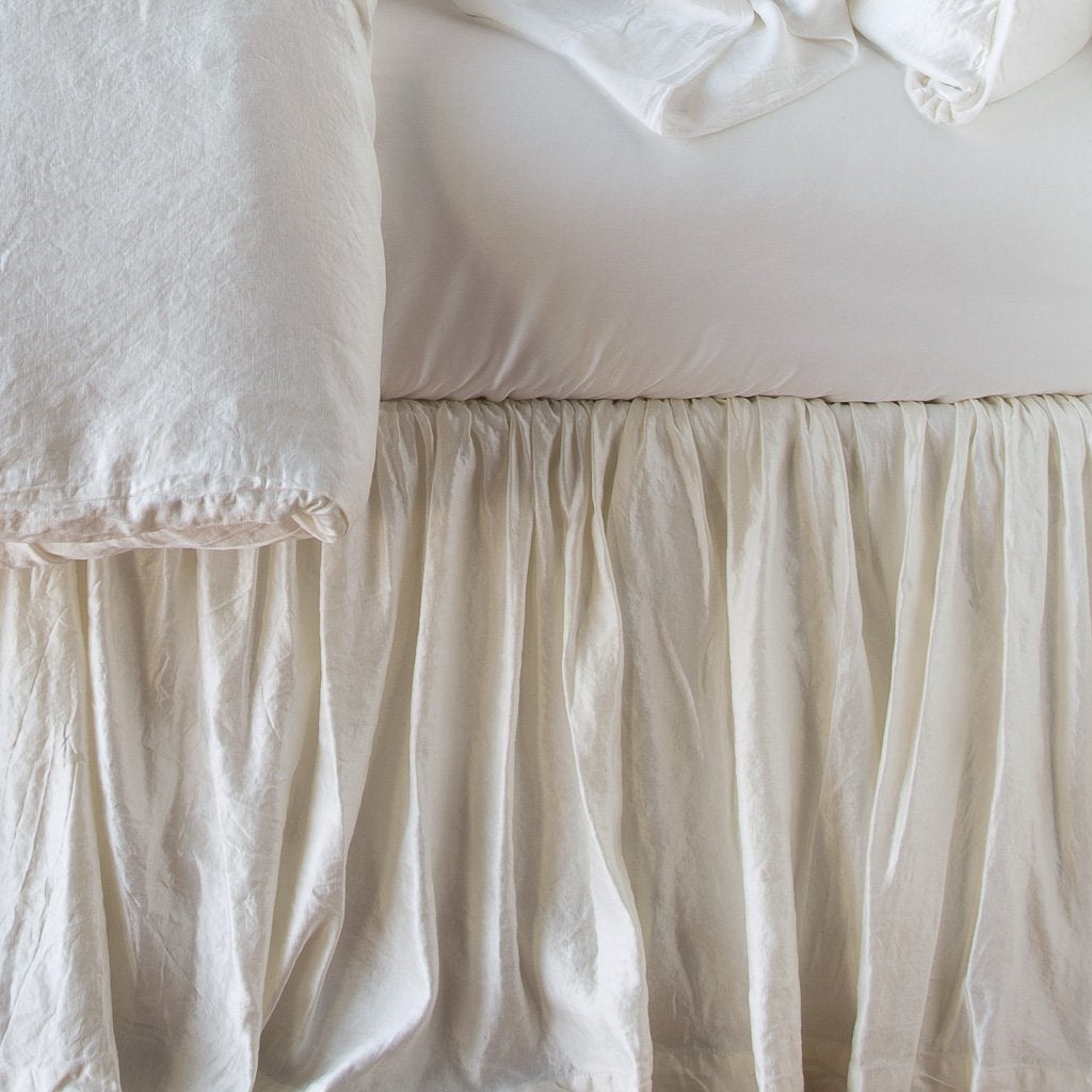 : Close up of Paloma bed skirt, highlighting the shimmering fabric and the gathering detail - winter white, side view.