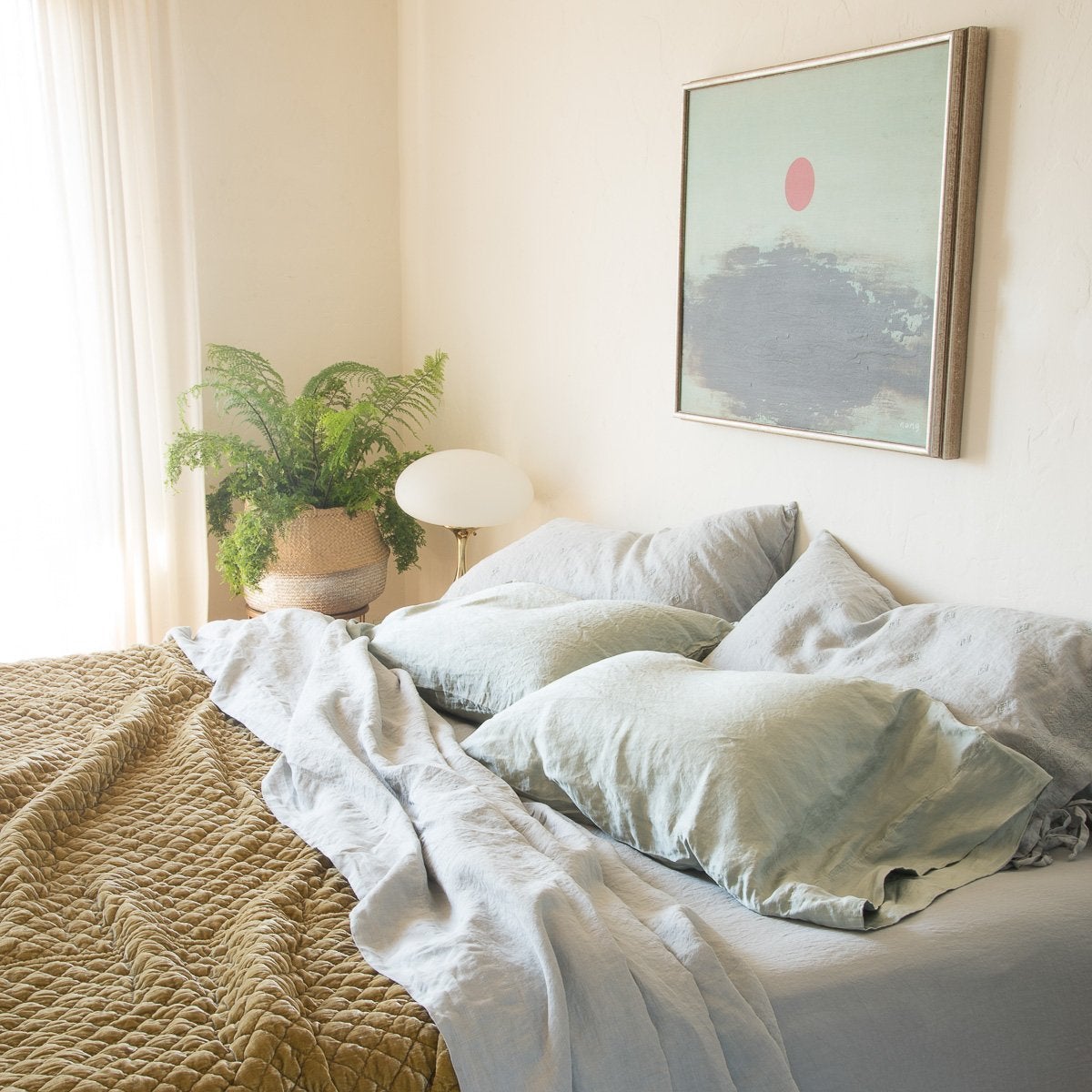 : Paloma sleeping pillows and linen sheets in pale mineral are paired with rich, golden, quilted silk velvet - cropped three-quarter angle.