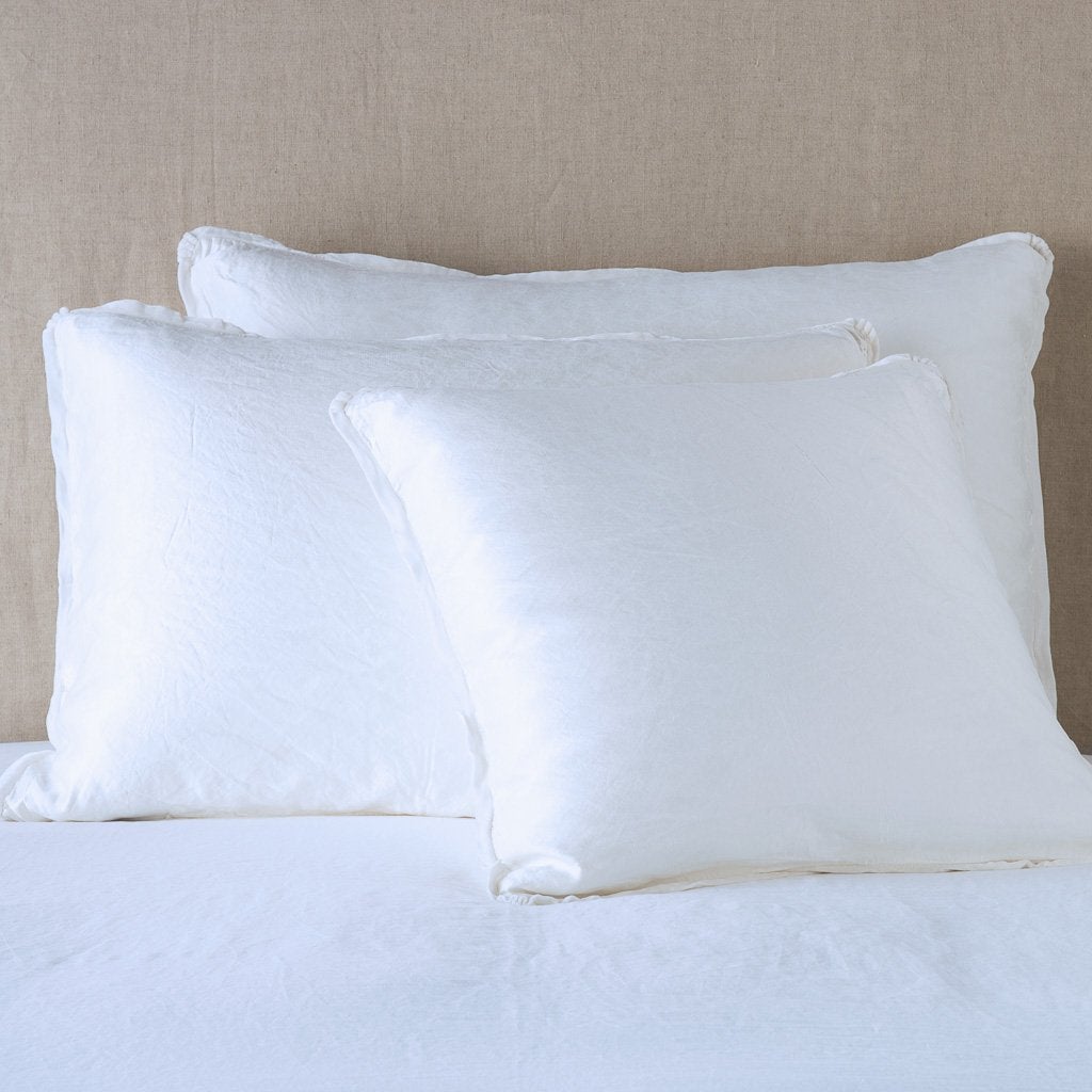 White: shams leaning upright on white sheeting against a neutral headboard.
