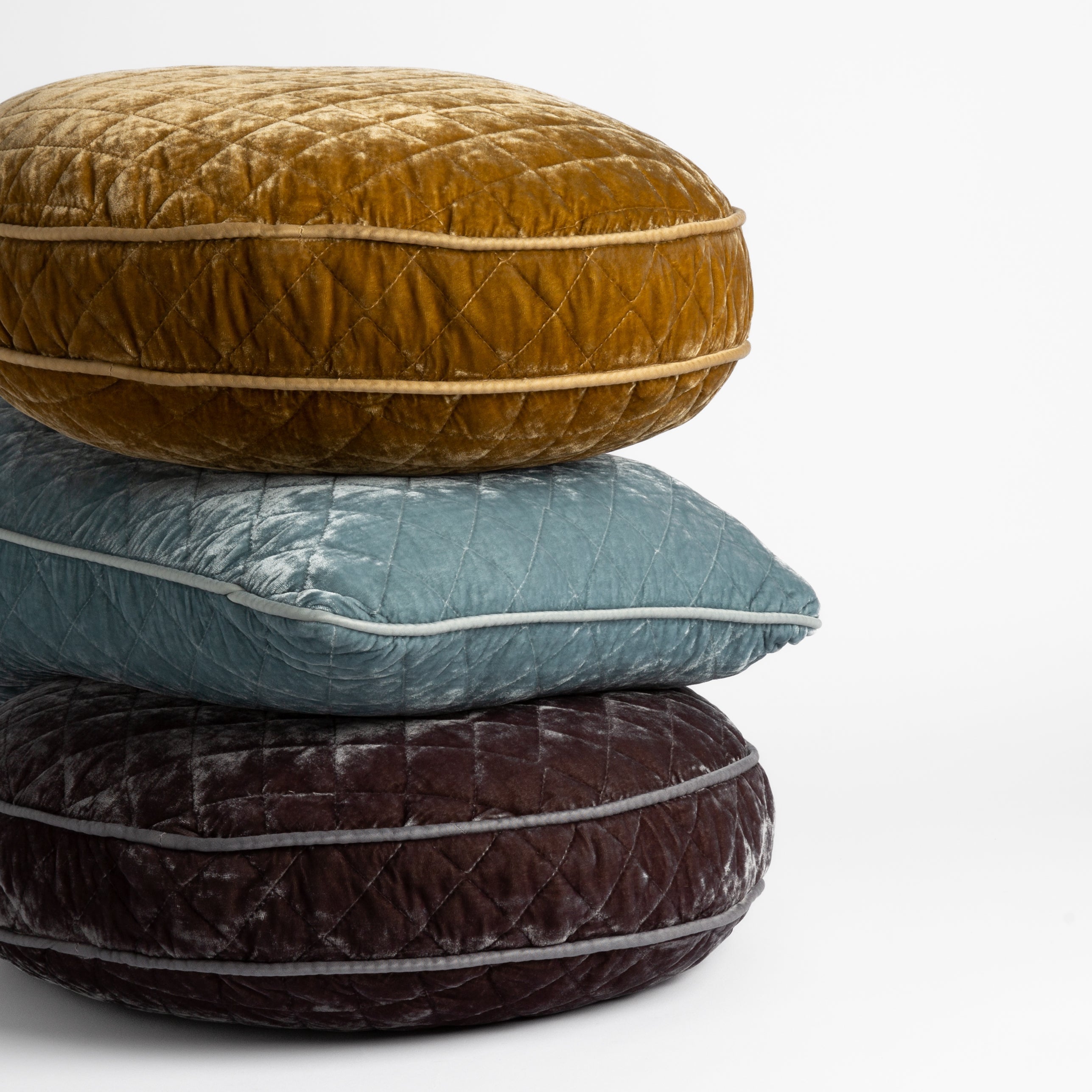 : Stack of silk vevlet quilted throw pillows show off shapes and satin piping details — honeycomb, clould and moonlight pillows straight on at a slight angle against a white.