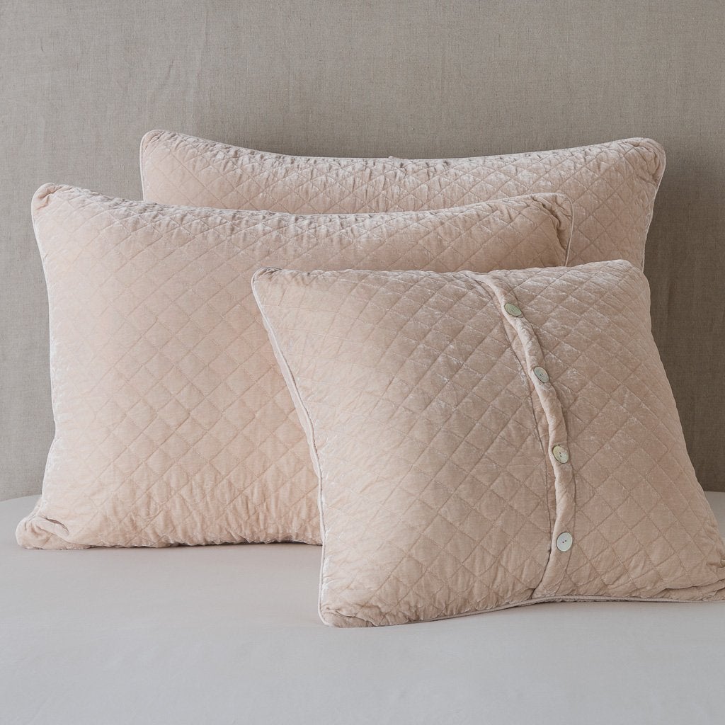 : Silk velvet quilted shams leaning upright against a neutral headboard. One sham is backwards to showcase the shimmering shell button closure - pearl.