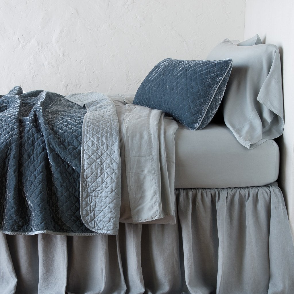 Mineral: throw blanket rumpled and folded back, featuring satin back. Shown with matching lumbar pillow and monochromatic sheeting - side view.