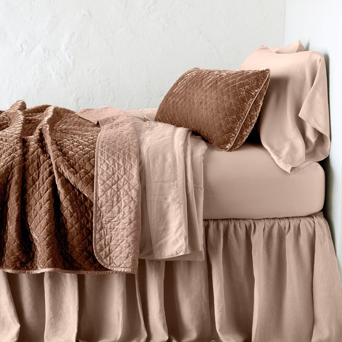 Rouge: throw blanket rumpled and folded back, featuring satin back. Shown with matching lumbar pillow and monochromatic sheeting - side view.