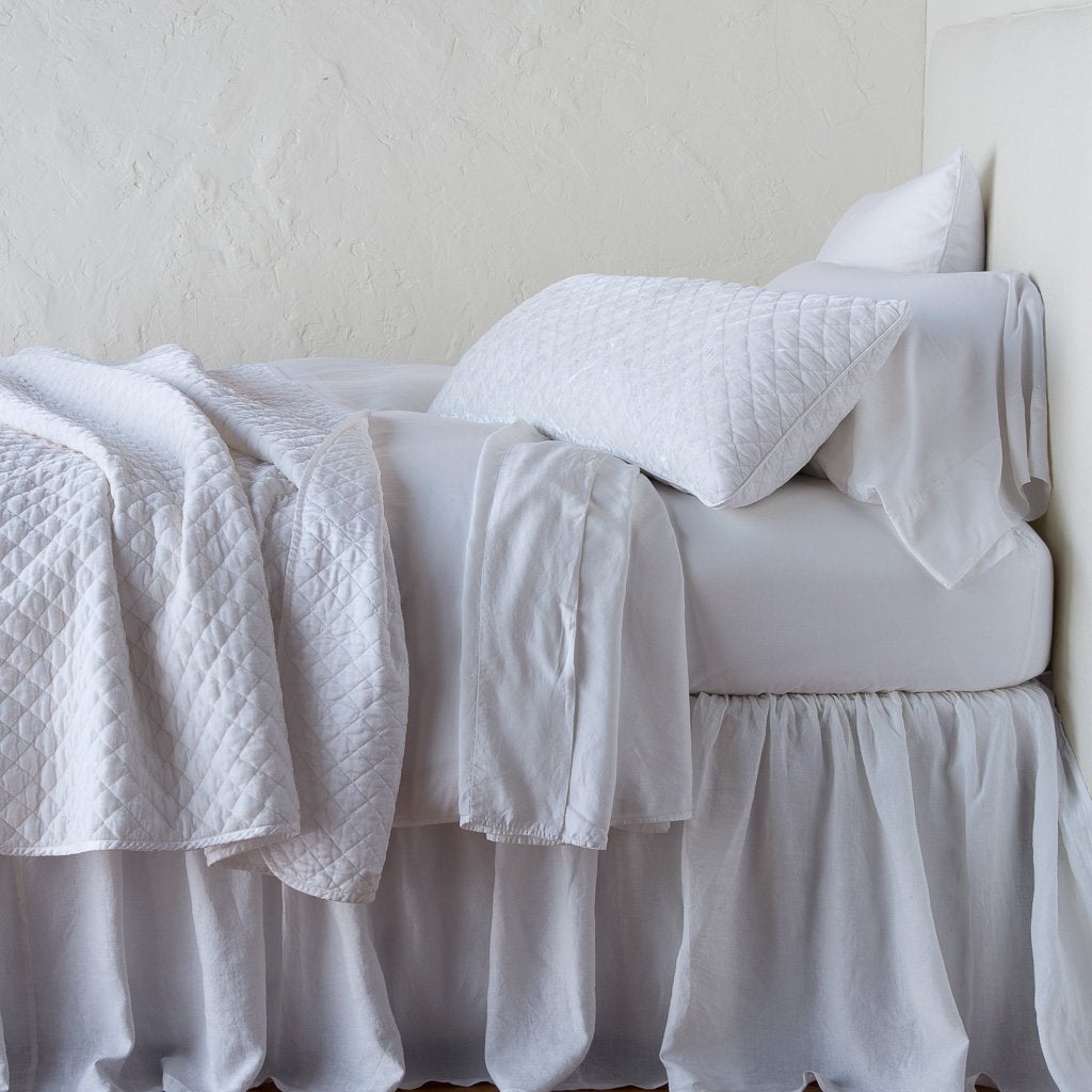 White: throw blanket rumpled and folded back, featuring satin back. Shown with matching lumbar pillow and monochromatic sheeting - side view.