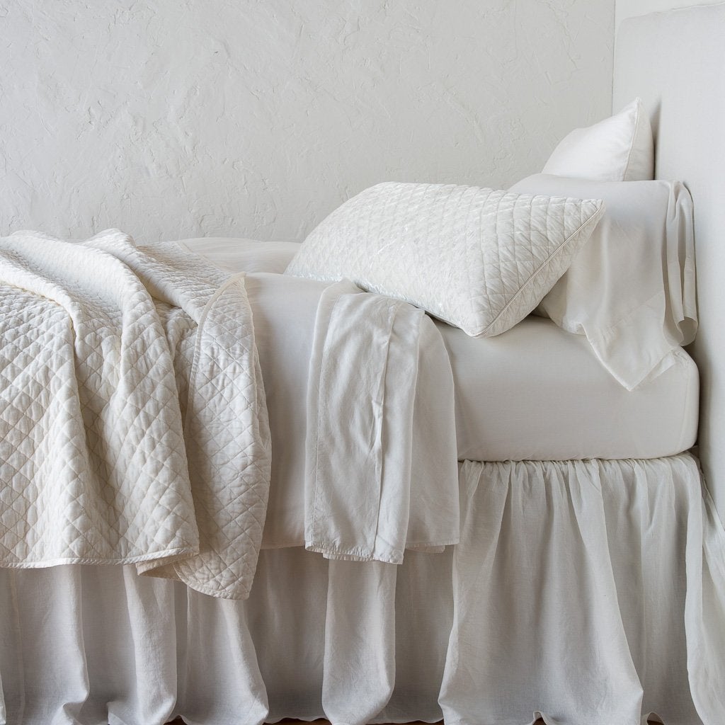 : Silk velvet throw blanket rumpled and folded back, featuring satin back. Shown with matching lumbar pillow and monochromatic sheeting - winter white, side view.