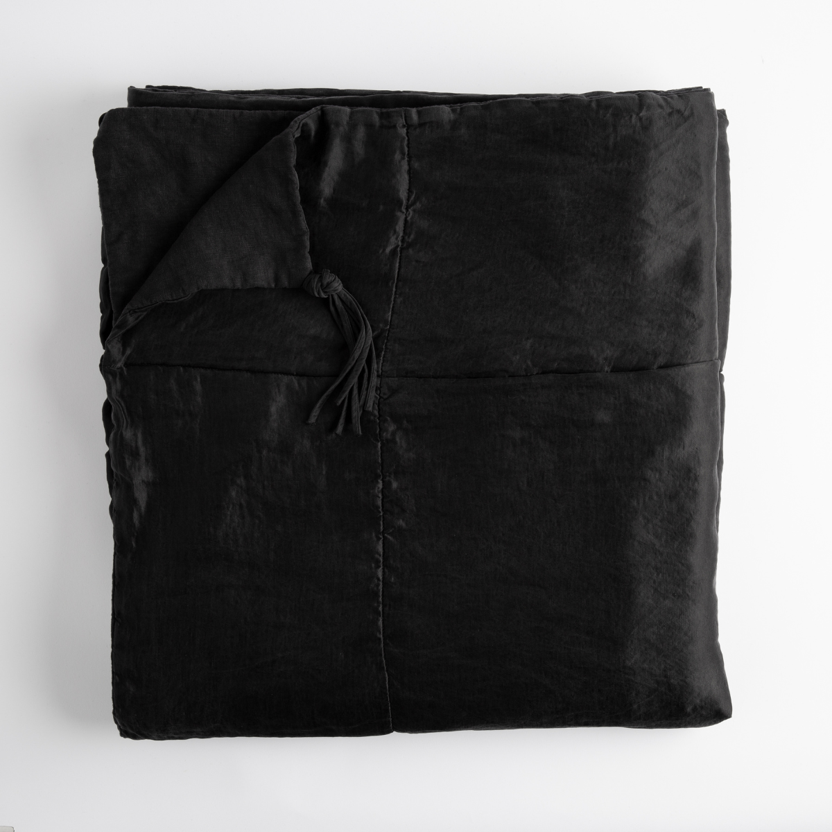 Corvino: folded bed blanket with corner folded downward showing linen back and tassel - overhead on white background.