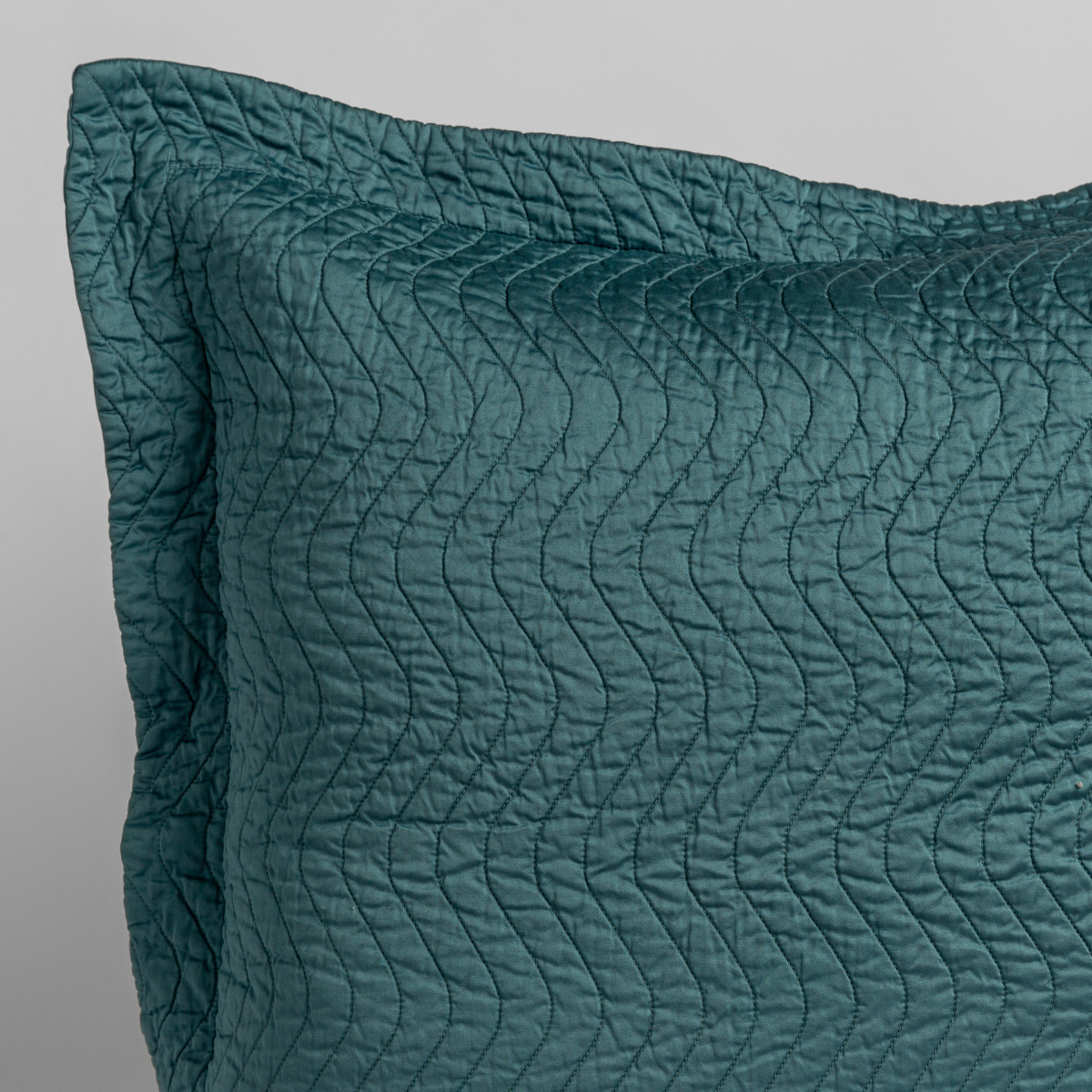 Cenote: a close up of a pillow corner showing the flange framing quilted cotton sateen shot against a white background. 