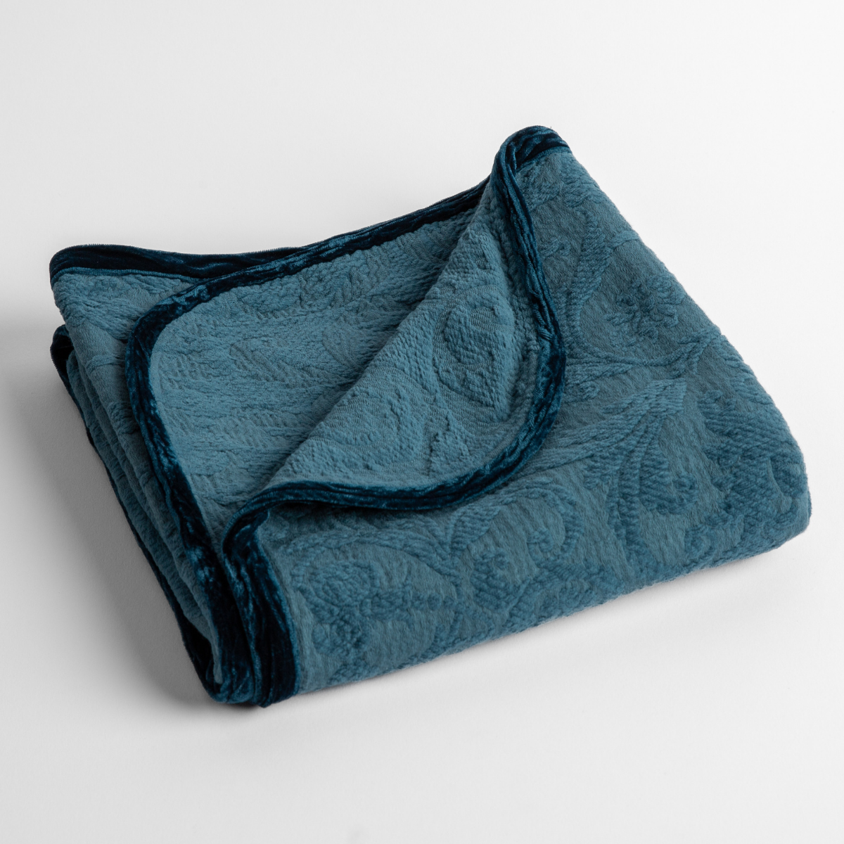 Cenote:  a folded blanket with the corner turned down to show the trim against a white background, shot from an overhead angle. 