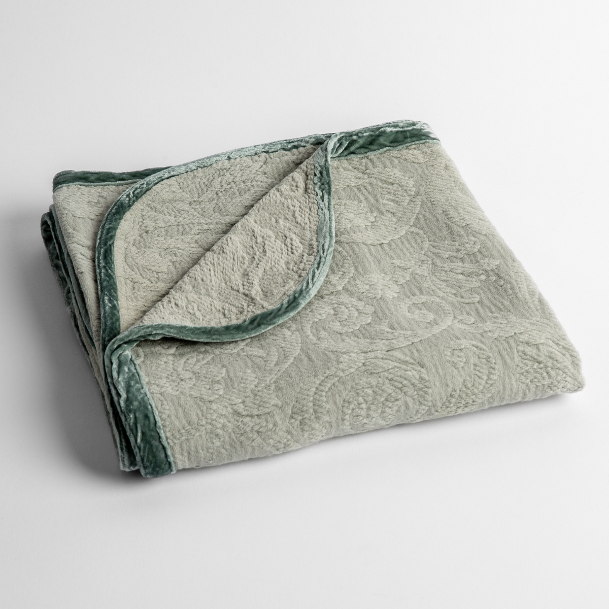 Eucalyptus: a folded blanket with the corner turned down to show the trim against a white background, shot from an overhead angle. 