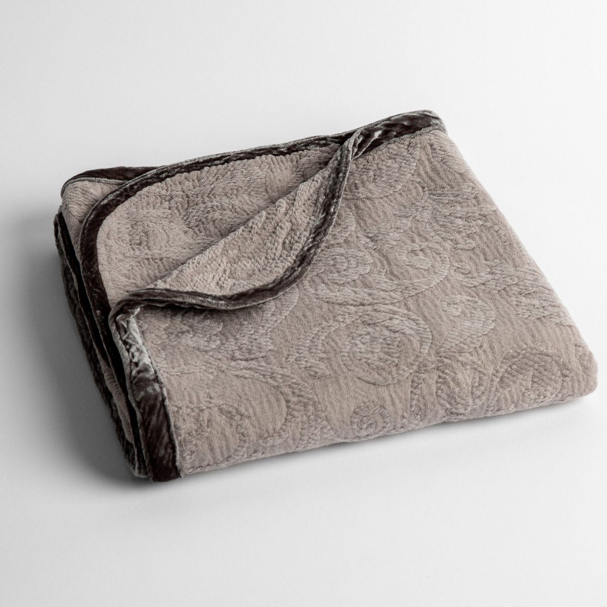 Fog: a folded blanket with the corner turned down to show the trim against a white background, shot from an overhead angle. 