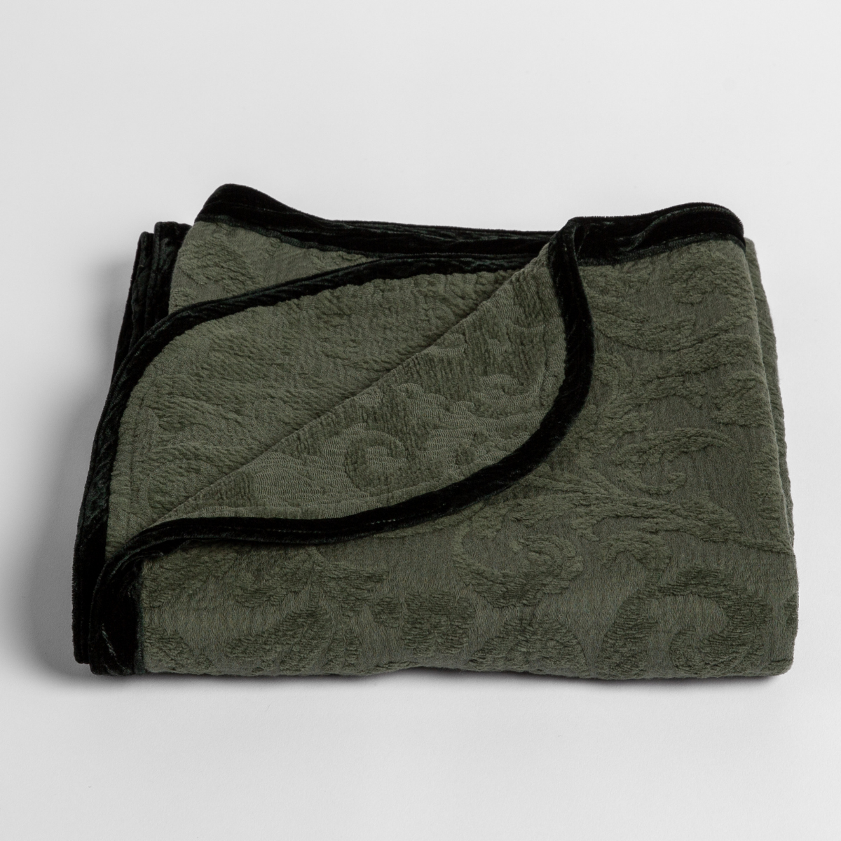 Juniper: a folded blanket with the corner turned down to show the trim against a white background, shot from an overhead angle. 