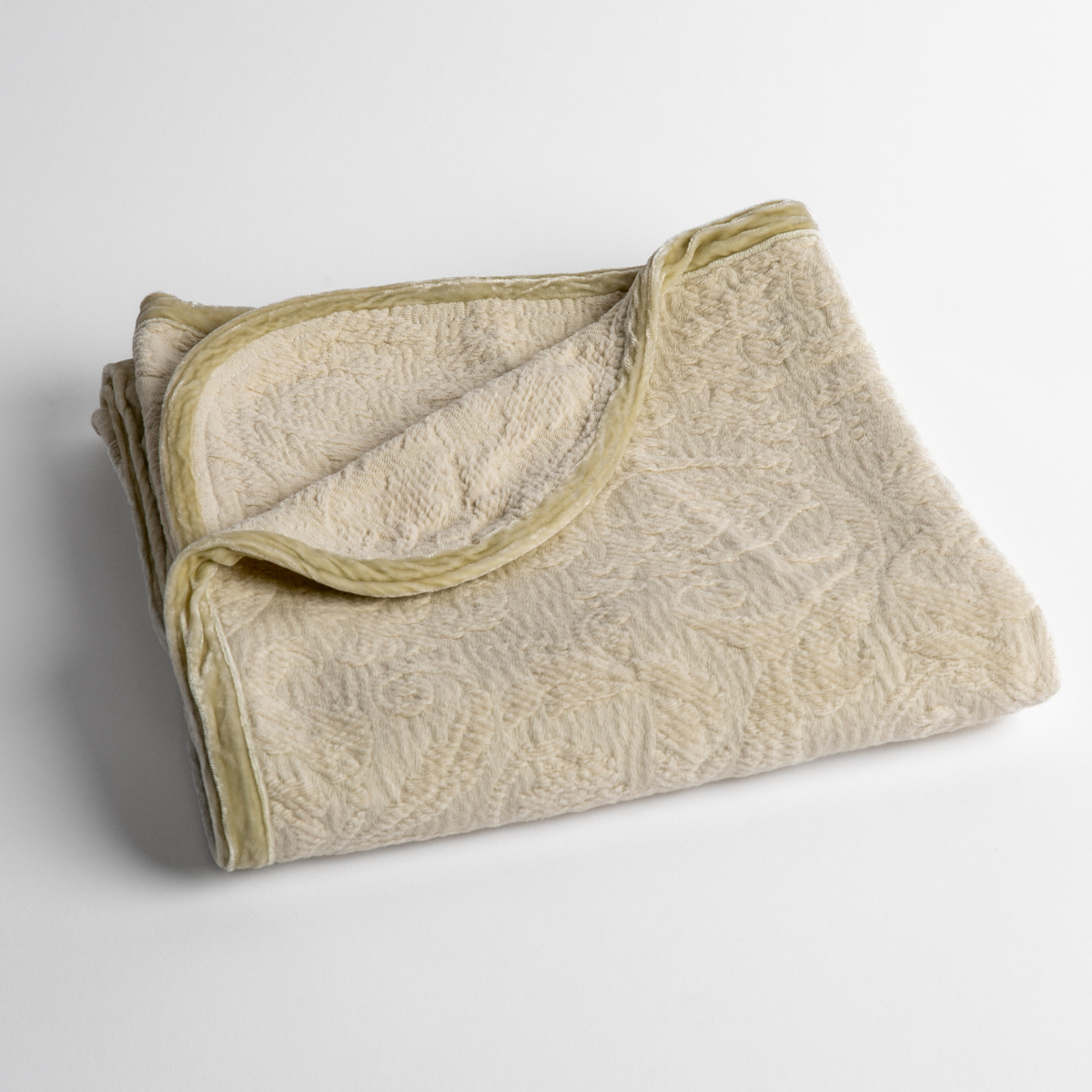 Parchment:  a folded blanket with the corner turned down to show the trim against a white background, shot from an overhead angle. 