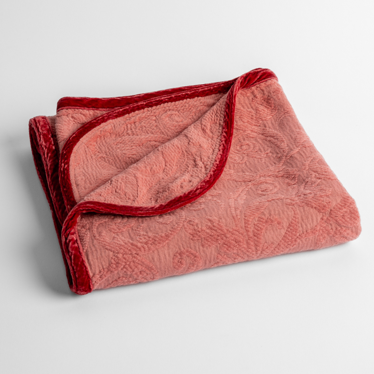 Poppy: a folded blanket with the corner turned down to show the trim against a white background, shot from an overhead angle. 