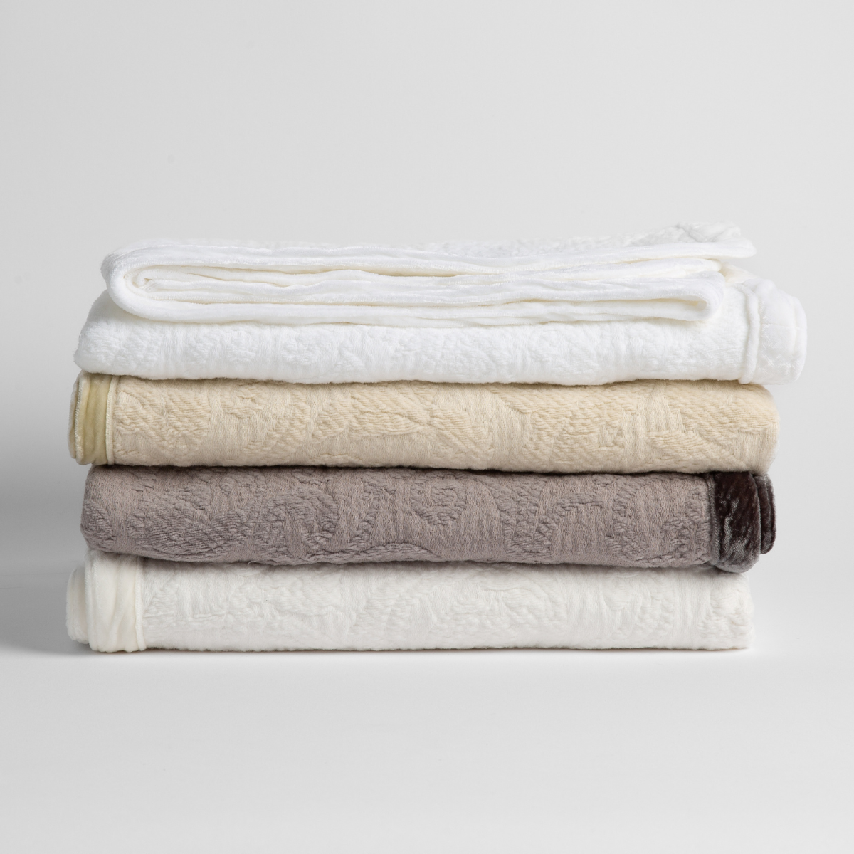 : a stack of four organic cotton baby blankets in white, parchment, moonlight and winter white.  against a white background. 